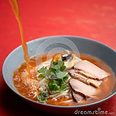Ramen soup is poured with broth. Bowl of noodles, meat and herbs parsley on red table. Spicy oriental dish, Pan-Asian Stock Photo