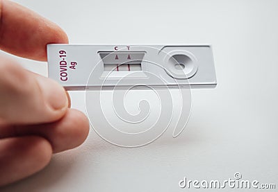 Rapid antigen detection test RADT with two red stripes showing a POSITIVE result of a human sample testing. Mans fingers holding Stock Photo