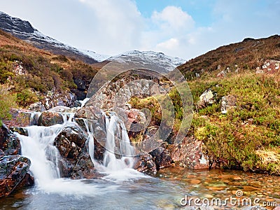 Rapids in small waterfall on stream, Higland in Scotland an early spring day. Snowy mountain peaks Stock Photo