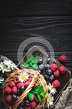 Raspberries and blueberries in a basket with chamomile and leaves on a dark background. Summer and healthy food concept Stock Photo