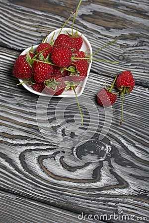 Raspberries with tails lie in a heart-shaped saucer. Several berries are nearby. On black boards, with an expressive woody texture Stock Photo