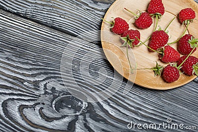 Raspberries with tails lie on a wooden saucer. On black boards, with an expressive woody texture Stock Photo