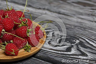 Raspberries with tails lie on a wooden saucer. On black boards, with an expressive woody texture Stock Photo