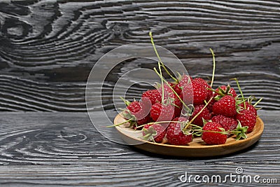 Raspberries with tails lie on a wooden saucer. On black boards, with an expressive woody texture Stock Photo