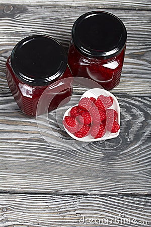 Raspberry jam in glass jars. Nearby are raspberries in a saucer. On wooden boards with a beautiful texture Stock Photo