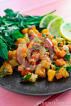 Ratatouille on a black plate, colored different vegetables in a stew, with fresh parsley leaves and lemon slices, on a pink wooden Stock Photo