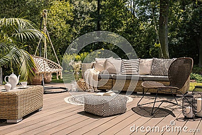 A rattan patio set including a sofa, a table and a chair on a wooden deck in the sunny garden. Stock Photo