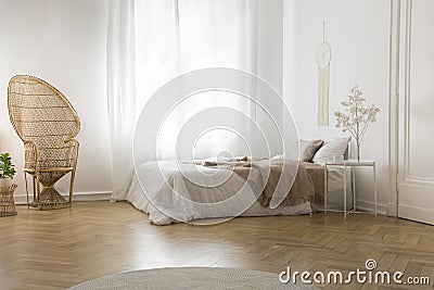 Rattan peacock chair next to window in white bedroom interior with blanket on bed Stock Photo