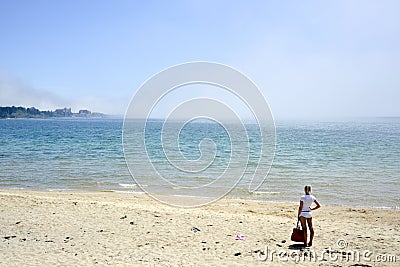 A lonely woman standing near waterfront looks at the seashore with misty clouds covering waves. Editorial Stock Photo