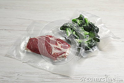 Raw beef and broccoli in vacuum packs on white wooden table Stock Photo