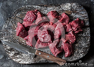 Raw beef fillet meat pieces for stew on a wooden rustic cutting board on dark background, top view Stock Photo