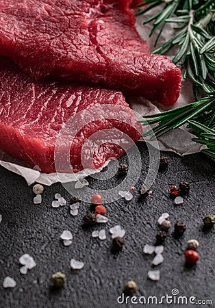 Raw beef steak with rosemary branches on parchment paper with pepper and salt Stock Photo