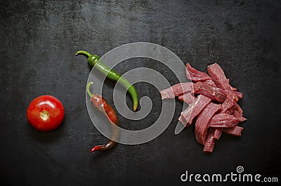 Raw beef strips, ripe tomato and hot pepper pods on black Stock Photo