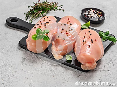 Raw chicken breast with fresh basil on black cuttingboard over cement background Stock Photo