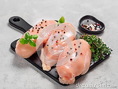 Raw chicken breast with fresh basil on black cuttingboard over cement background Stock Photo