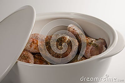 Raw chicken drumsticks marinated in spices in a large white ceramic saucepan with a lid Stock Photo