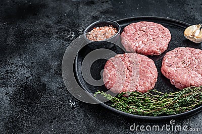 Raw chicken turkey patty, minced meat cutlets on a plate with thyme. Black background. Top view. Copy space Stock Photo