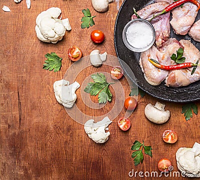 Raw chicken wings with red pepper and salt pans, cast iron with tomatoes and cauliflower on rusti? wooden background top view clo Stock Photo
