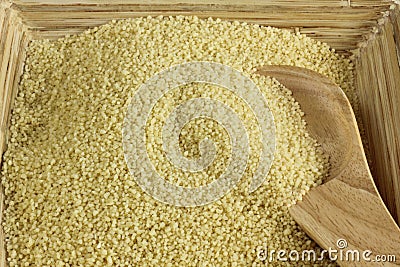 Raw couscous with wooden spoon in wooden bowl Stock Photo