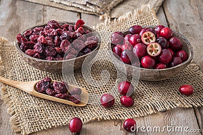 Raw and dried cranberries in coconut shells and on a wooden spoon on wooden table Stock Photo