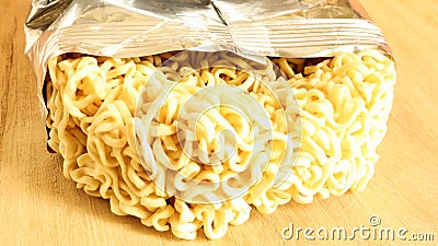 Raw dried instant noodles on a round wooden cutting board in an unnamed foil packaging with no name close up on a yellow Stock Photo