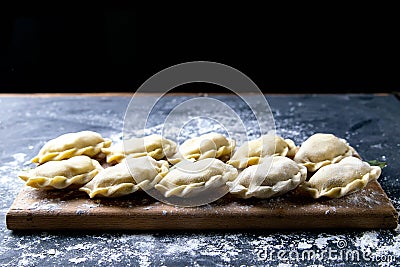 Raw dumpling with potatoes. Preparation dumplings on a wooden board on dark background. Top views, close-up Stock Photo