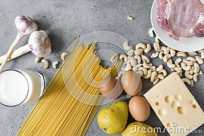 Raw eggs, Maasdam cheese, cashew nuts, glass of milk, pasta , pears, piece of raw pork, meat, garlic on grey background Stock Photo