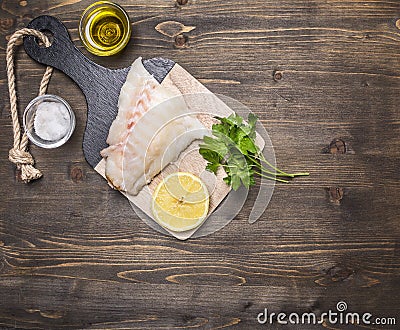 Raw fish fillet on a cutting board with lemon, herbs, butter and salt border ,place for text wooden rustic background top view Stock Photo