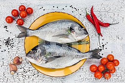 Raw fresh dorado fish on yellow plate and vegetables on white table. Top view. Stock Photo