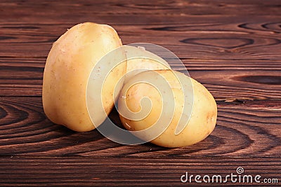 Raw, fresh and uncooked potatoes on a dark brown wooden background. Fresh vegetables. Raw, clean and light brown new potatoes. Stock Photo