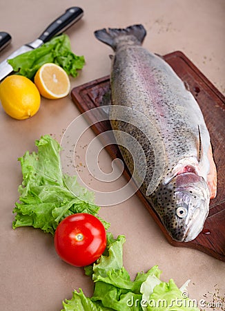 Raw fresh unprepared salmon fish on a wooden board with ingredients for cooking. Lemon, lettuce, tomatoes. Stock Photo