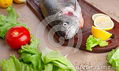 Raw fresh unprepared salmon fish on a wooden board with ingredients for cooking. Lemon, lettuce, tomatoes. Stock Photo