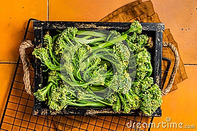 Raw green baby Broccolini in a wooden tray. Orange background. Top view Stock Photo