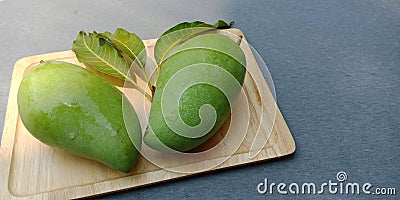 Raw green mango fruit on wooden plate Stock Photo