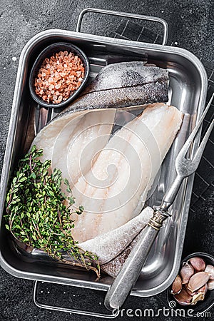 Raw haddock fish fillets, whitefish meat in kitchen tray with thyme. Black background. Top view Stock Photo