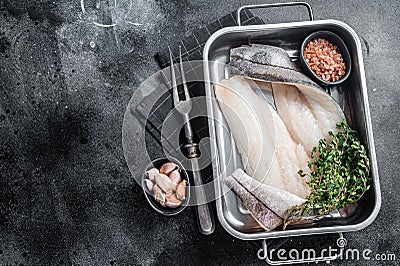 Raw haddock fish fillets, whitefish meat in kitchen tray with thyme. Black background. Top view. Copy space Stock Photo