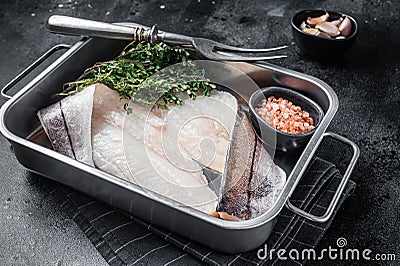 Raw haddock fish fillets, whitefish meat in kitchen tray with thyme. Black background. Top view Stock Photo