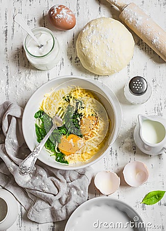 Raw ingredients for baking a pie with spinach - eggs, cheese, dough, spinach, cream on light wooden background. Stock Photo