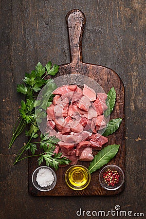 Raw ingredients for stew. pork meat cubes, oil ,salt and fresh seasoning on old rustic cutting board on dark wooden background top Stock Photo