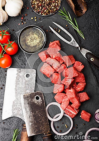 Raw lean diced casserole beef pork steak with vintage meat hatchet and fork on stone background. Salt and pepper with fresh Stock Photo