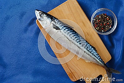 Raw mackerel fish whole, on a cutting board, bowl with a mixture of peppers and spices and a blue satin tablecloth. Top view with Stock Photo