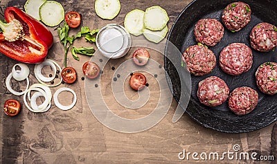 Raw meat balls in vintage cast-iron pan with tomatoes, onions and peppers, herbs on wooden rustic background top view close up Stock Photo