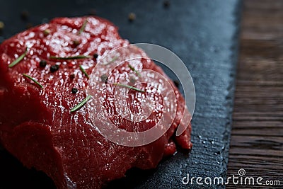 Raw meat beef steaks on black slate board with spices and rosemary over wooden background, copy space Stock Photo