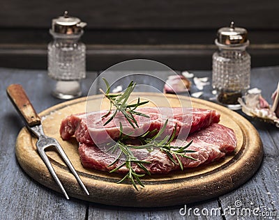 Raw meat with rosemary, garlic, salt and pepper on a wooden board with a fork Stock Photo