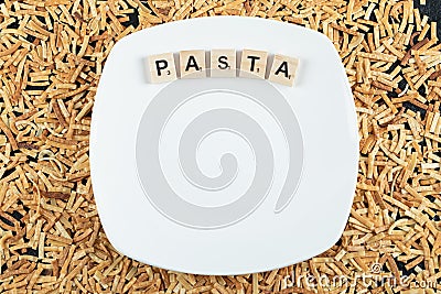 Raw pasta scattered around white plate with wooden letters Editorial Stock Photo