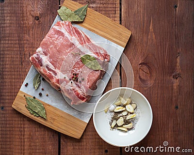 Raw pork in specials and a plate with chopped garlic and ground pepper stand on a wooden table Stock Photo