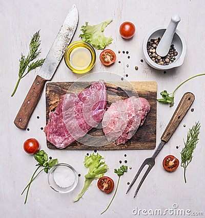 Raw Pork steak with vegetables and herbs, meat knife and fork, on a cutting board wooden rustic background top view close up Stock Photo