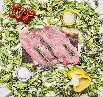 Raw pork steak on vintage cutting board with lettuce, cherry tomatoes, bell pepper, oil spices wooden rustic background top Stock Photo