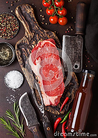 Raw sirloin beef steak on vintage chopping board with knife and fork on rusty background. Salt and pepper with fresh rosemary and Stock Photo