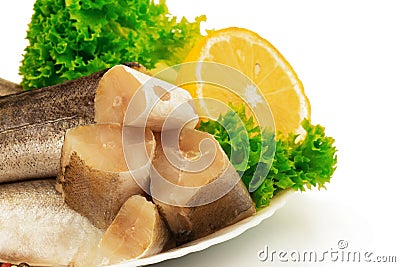 Raw slices of fish hake, pollock on the plate with lemon and leaves of salad lettuce on white background Stock Photo